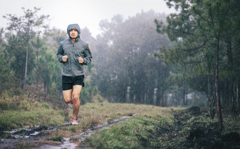 athlete runner in grey sports jacket forest trail in the rain